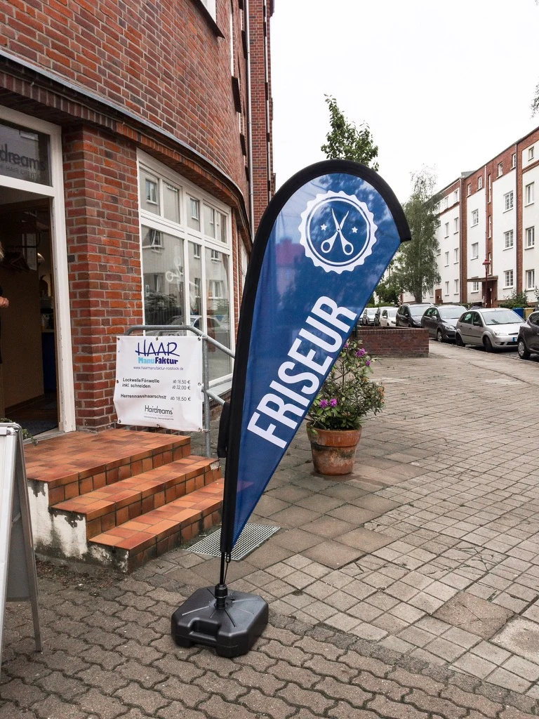 Beachflag mit Friseurmotiv vor einem Geschäft